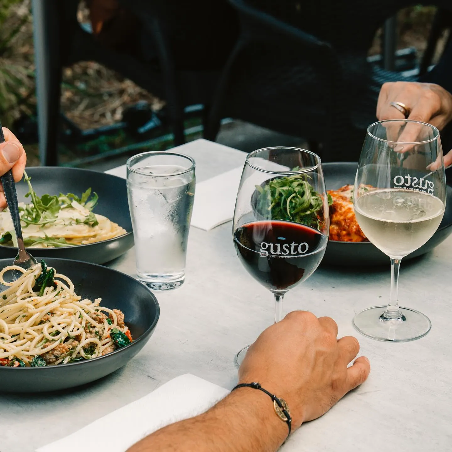 Diners sharing pasta with glasses of red and white wine at an outdoor table