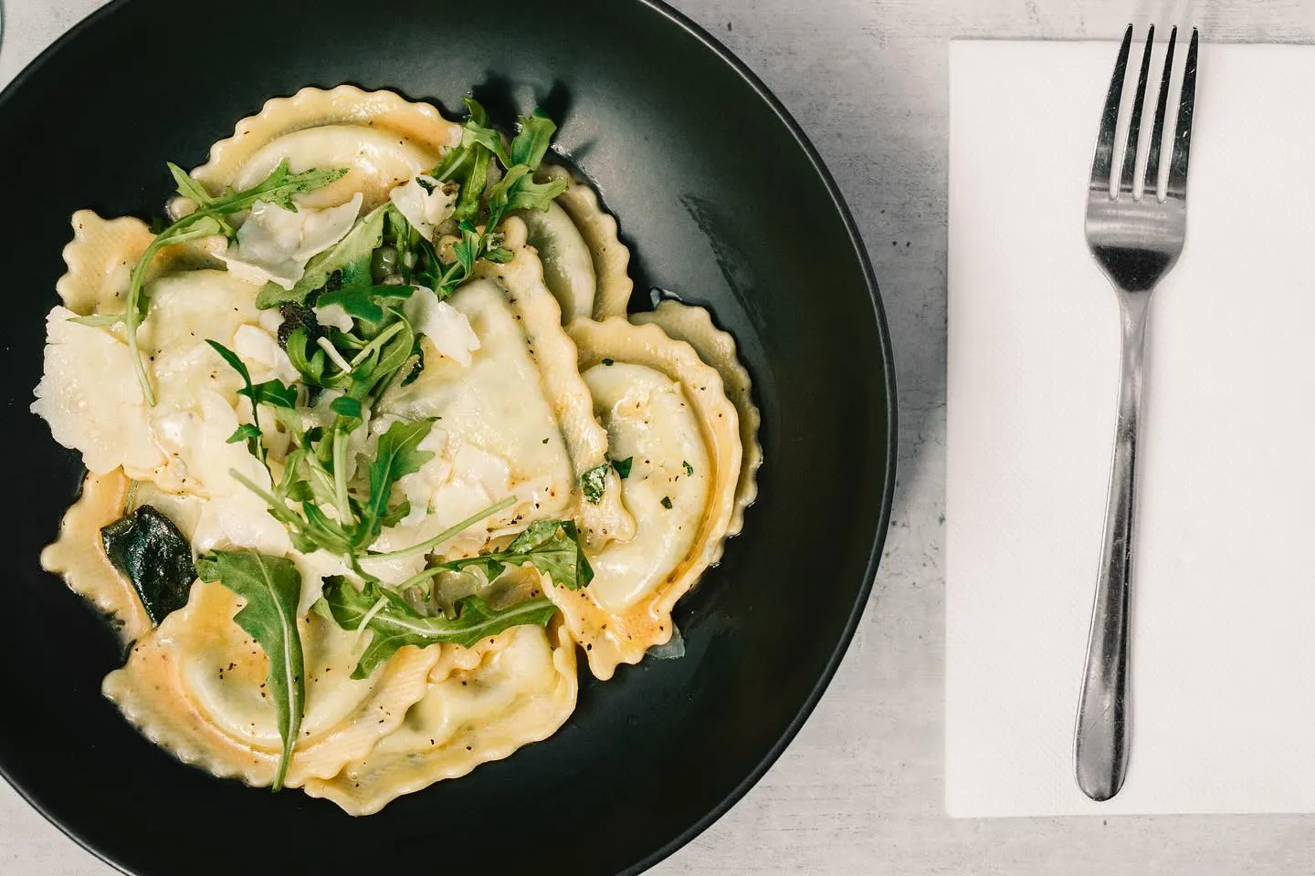 Ravioli topped with rocket and shaved parmesan in a butter sauce