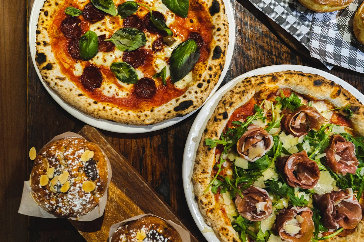 Overhead of pepperoni-basil pizza and prosciutto-rocket pizza with shaved parmesan, with almond-topped muffins